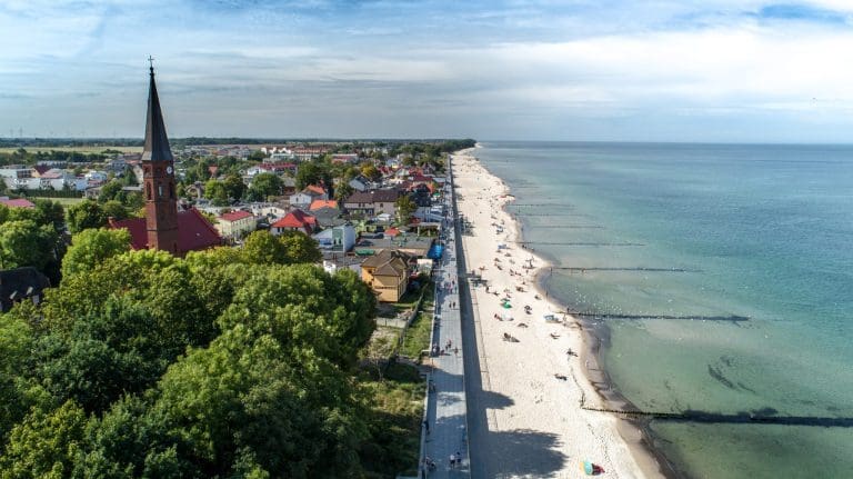 Plaża w Sarbinowie z lotu ptaka w sezonie letnim - szeroki pas piasku z plażowiczami i parawanami przy linii wody