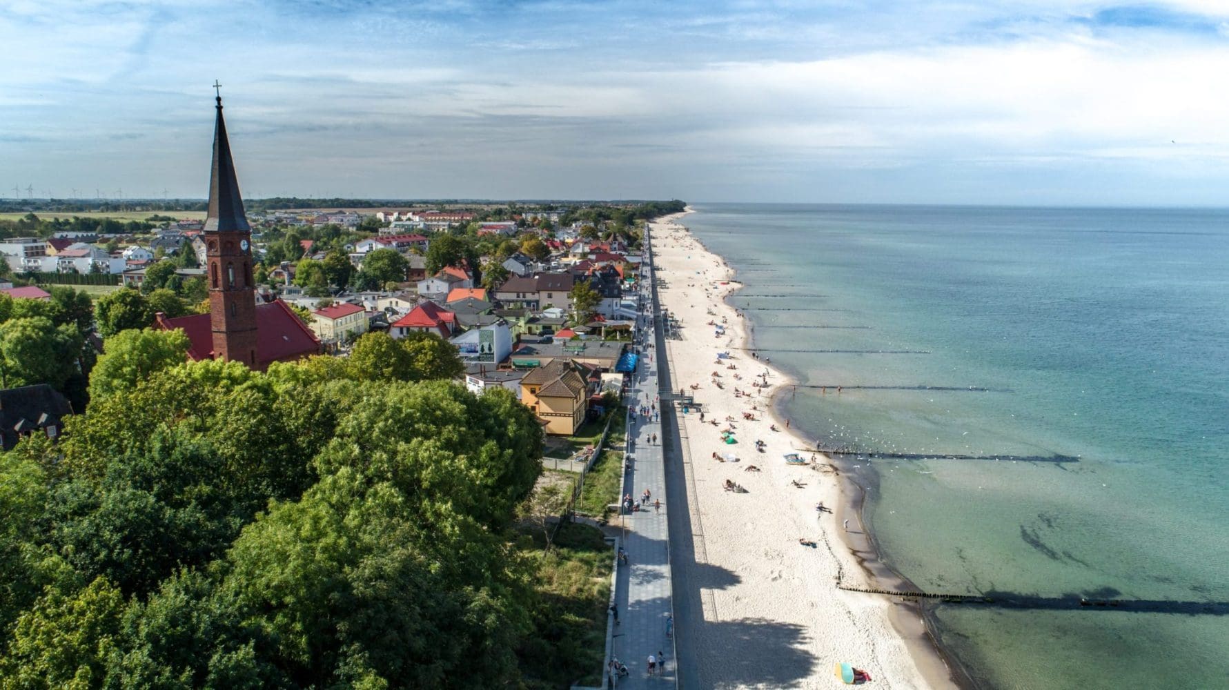 Plaża w Sarbinowie z lotu ptaka w sezonie letnim - szeroki pas piasku z plażowiczami i parawanami przy linii wody