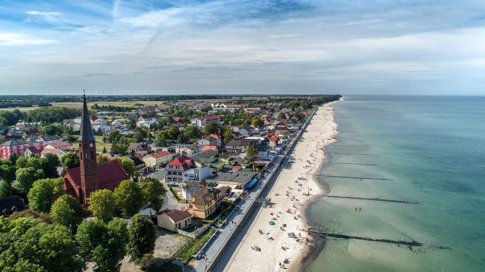 Plaża i morze z lotu ptaka, w tle kościół i zabudowa nadmorskiej wsi