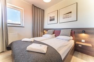 Zaścielone łóżko w apartamencie Wczasowa 8, w tle okno z widokiem na niebo