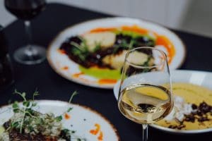 Zastawiony ciemny stół: kilka talerzy z daniami i kieliszki wina w ciepłym świetle.