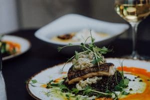 Smażona ryba z dodatkami i kieliszek białego wina na stole w restauracji Dobre Smaki
