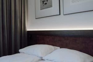 Sypialnia apartamentu wieczorem: podświetlony zagłówek i ciepłe światło nad łóżkiem.