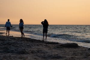 Trzy osoby przy linii wody na plaży w Sarbinowie o zachodzie słońca