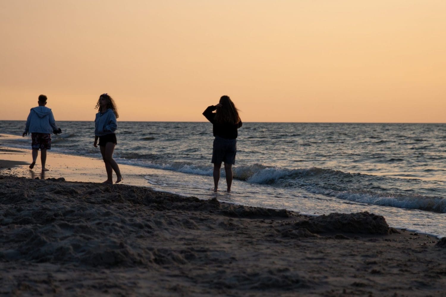 Trzy osoby przy linii wody na plaży w Sarbinowie o zachodzie słońca