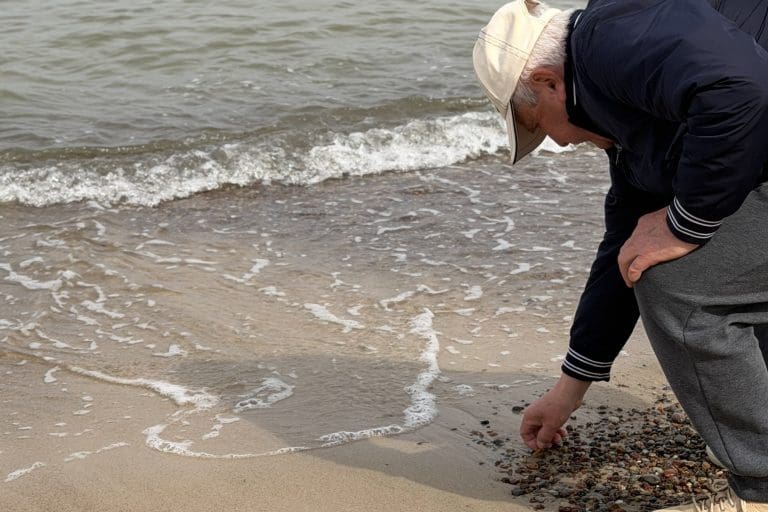 Mężczyzna schylony nad linią wody zbiera kamyki z mokrego piasku na plaży w Sarbinowie