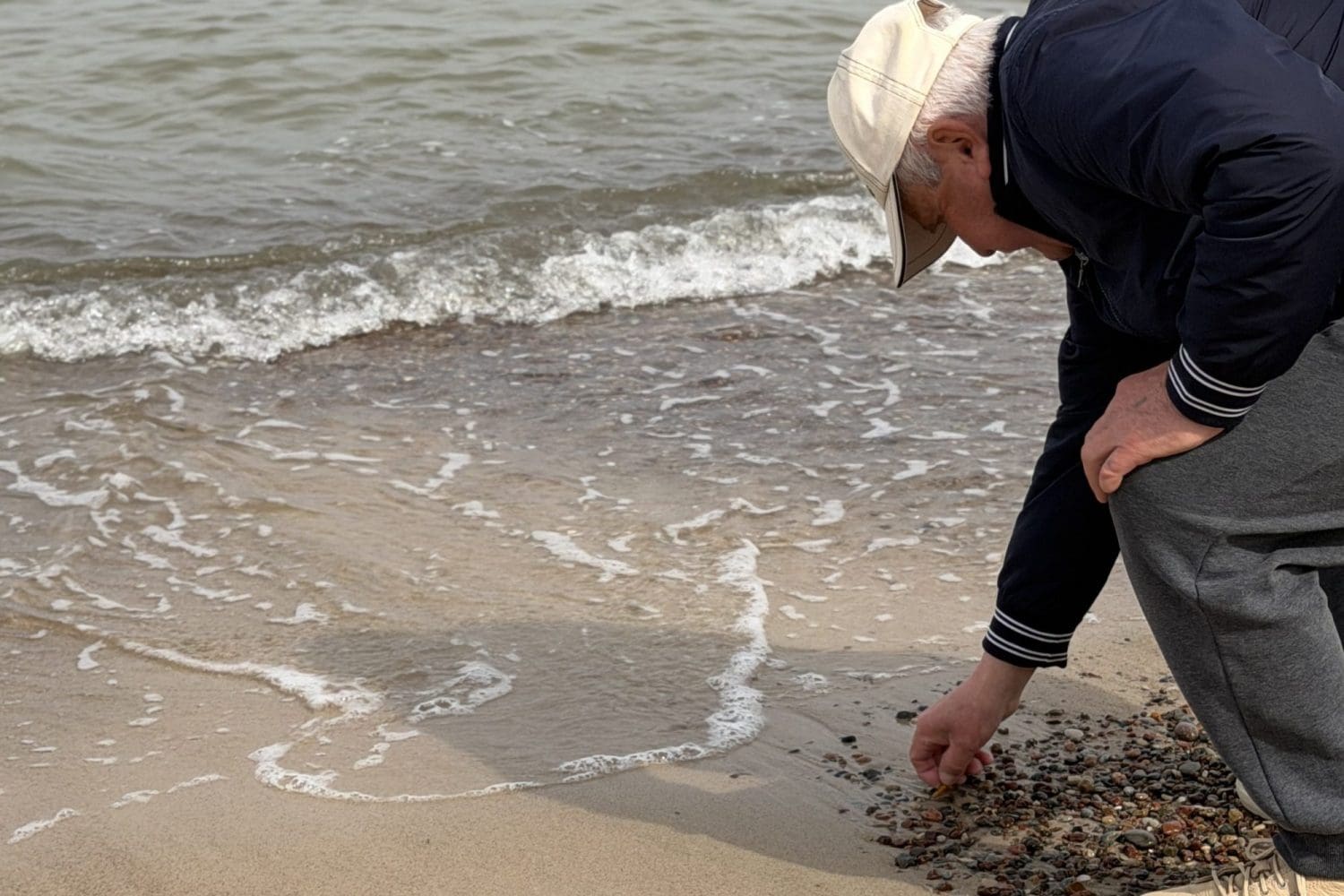 Mężczyzna schylony nad linią wody zbiera kamyki z mokrego piasku na plaży w Sarbinowie
