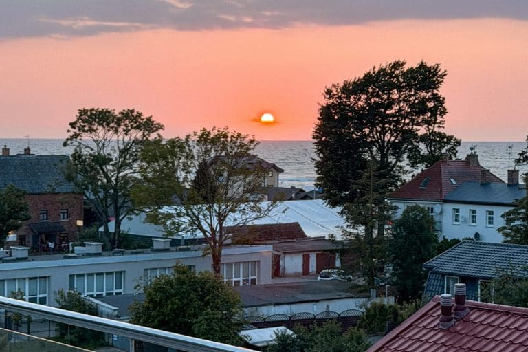 Słońce tuż nad horyzontem gaśnie nad morzem, w dole dachy Sarbinowa.