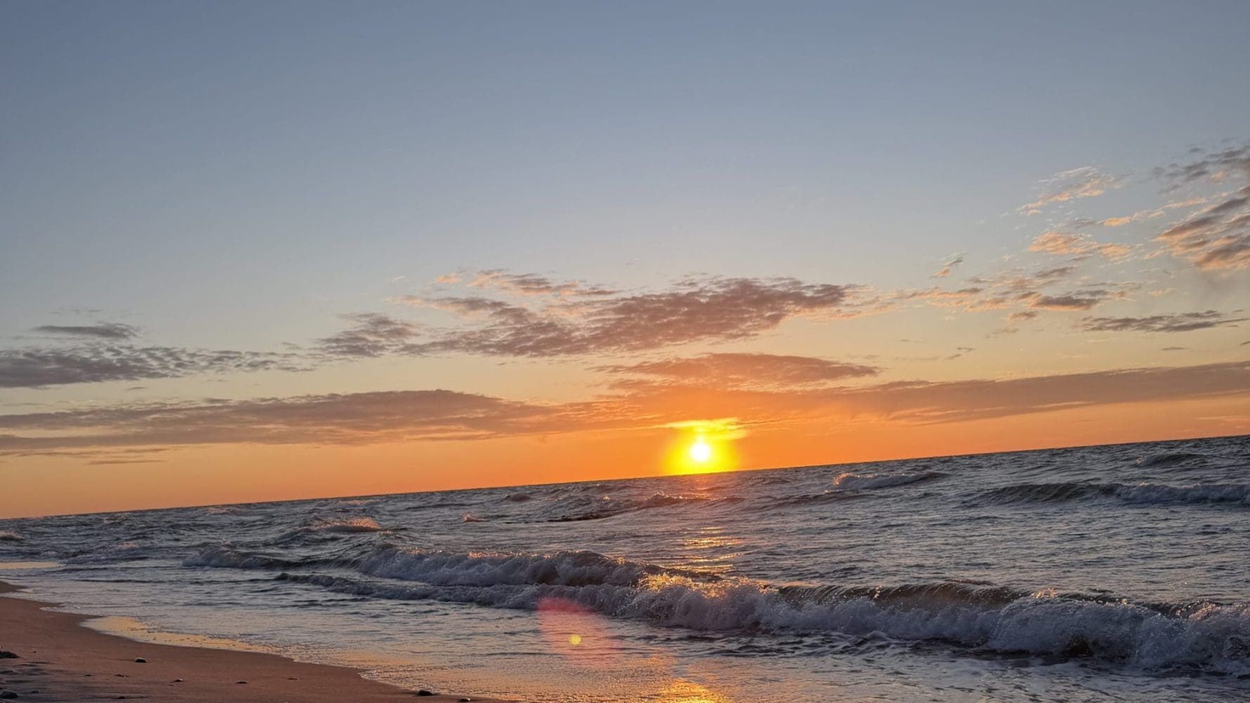 Słońce nisko nad horyzontem Bałtyku i pusta plaża w Sarbinowie