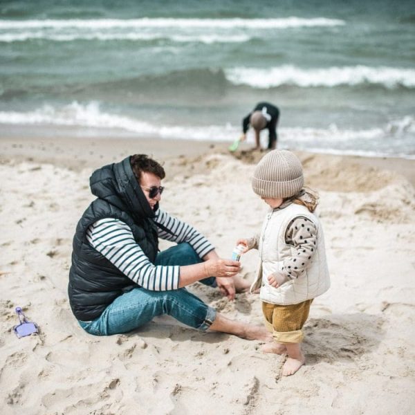 Tata z małym dzieckiem w czapce bawią się w piasku na plaży nad Bałtykiem