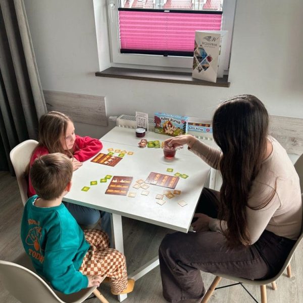 Mama z dziećmi gra w planszówkę przy stole w apartamencie