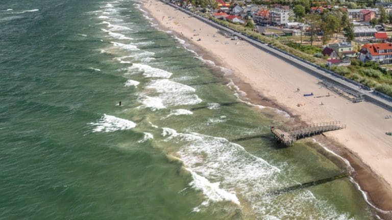 Plaża w Sarbinowie z lotu ptaka: linia brzegu Bałtyku, drewniany pomost i pojedynczy spacerowicze
