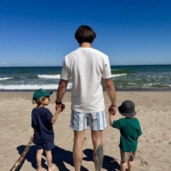 Tata z dwójką synów stoi na plaży i patrzy na morze w słoneczny dzień