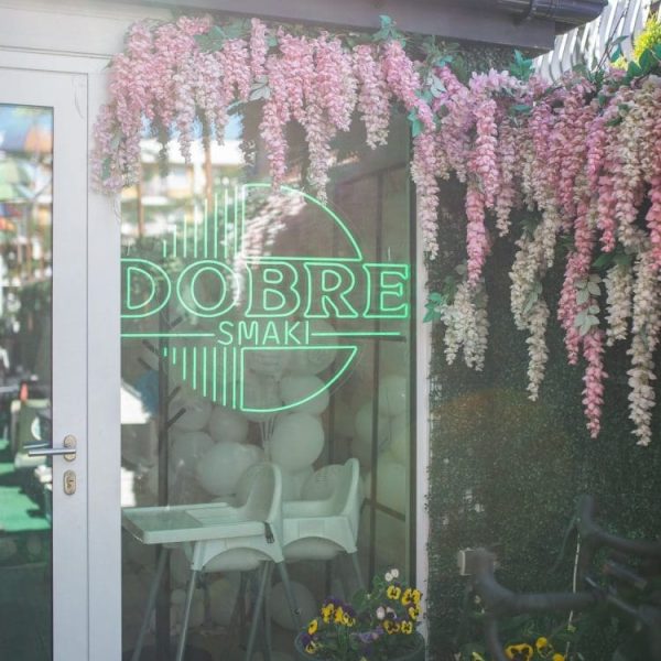 Wejście do restauracji Dobre Smaki z zielonym neonem i dekoracją kwiatową