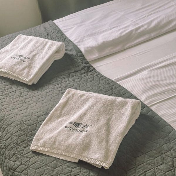 Ręczniki z haftowanym logo Wczasowej 8 przygotowane na łóżku w apartamencie