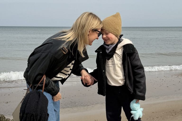 Roześmiana mama i synek w czapce stykają się czołami na plaży nad Bałtykiem.