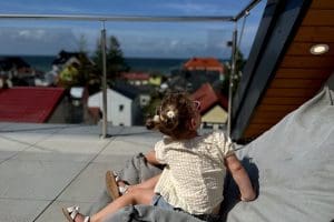 Dziewczynka odpoczywa na dużej pufie na słonecznym tarasie widokowym i patrzy na dachy Sarbinowa i morze.