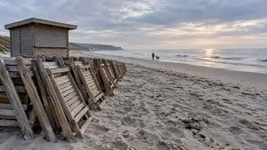 Pusta plaża po sezonie: ułożone w stos leżaki i zamknięty kiosk, w oddali mieszkaniec spaceruje z psem
