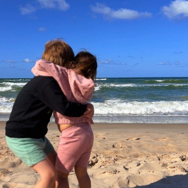 Dwoje dzieci przytula się na plaży, za nimi fale Bałtyku