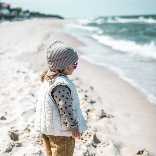 Dziecko w czapce i kamizelce na plaży przy brzegu morza