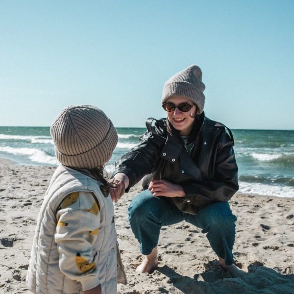 Mama bawi się z dzieckiem na plaży, oboje w ciepłych czapkach