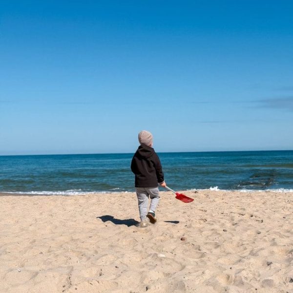 Dziecko z czerwoną łopatką idzie po plaży w stronę morza