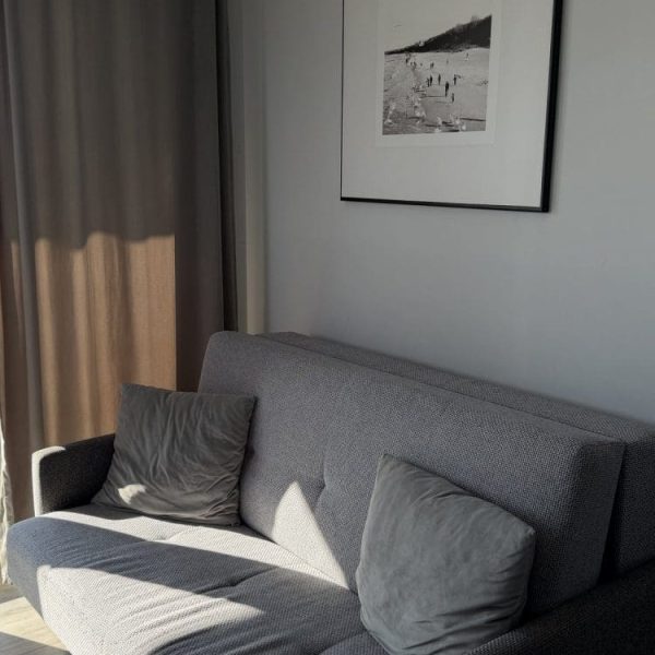 Salon apartamentu we Wczasowej 8 z szarą sofą w popołudniowym słońcu
